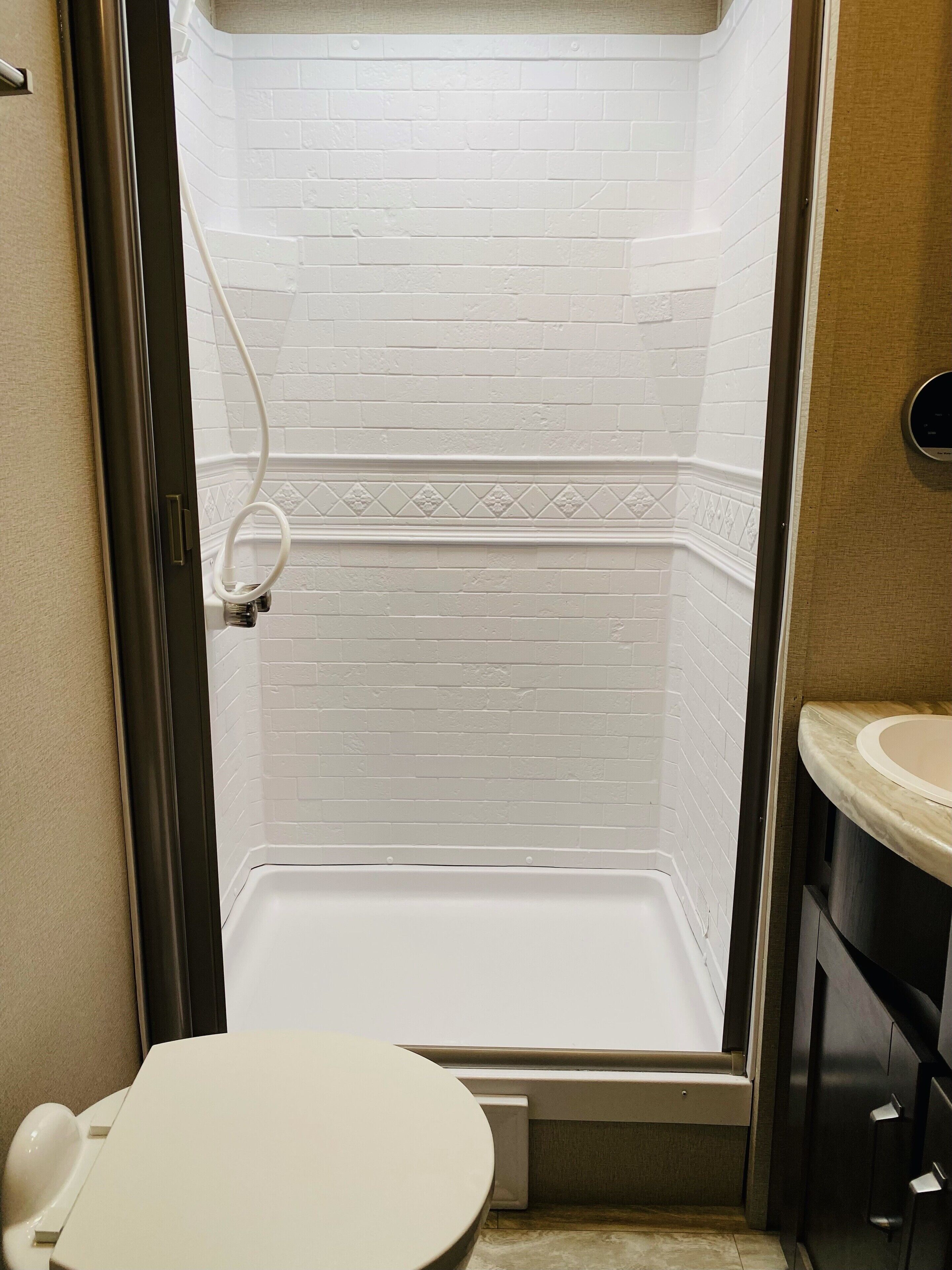 Une salle de bain avec une douche carrelée de carreaux blancs, des toilettes et un meuble-lavabo avec un évier.