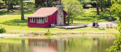 A red building with a stone chimney, located near a pond with a dock.