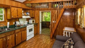 A rustic cabin interior with a kitchen, dining area, and a loft bedroom.