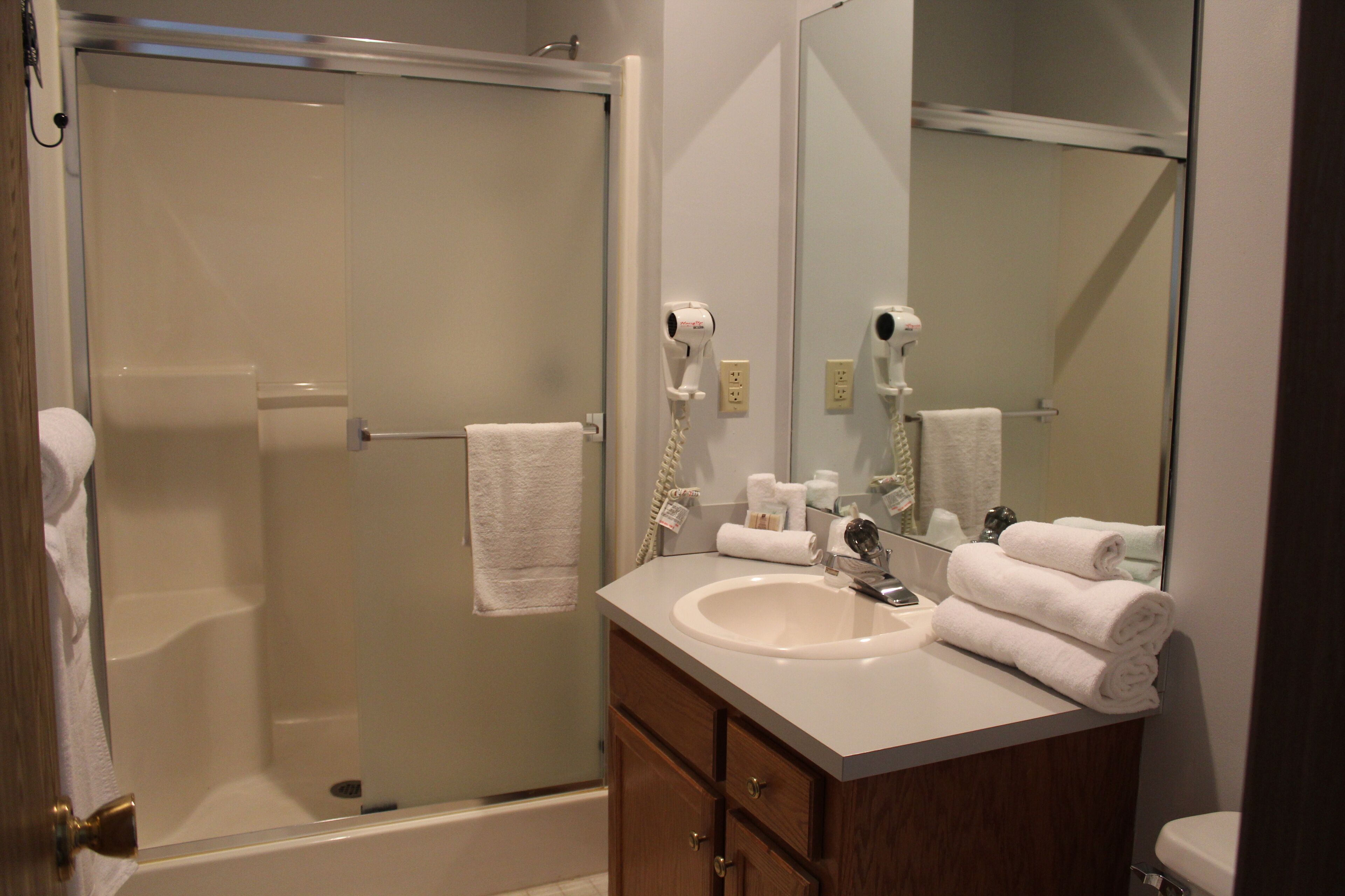 A bathroom with a glass-enclosed shower, a sink with a mirror, and neatly folded towels.