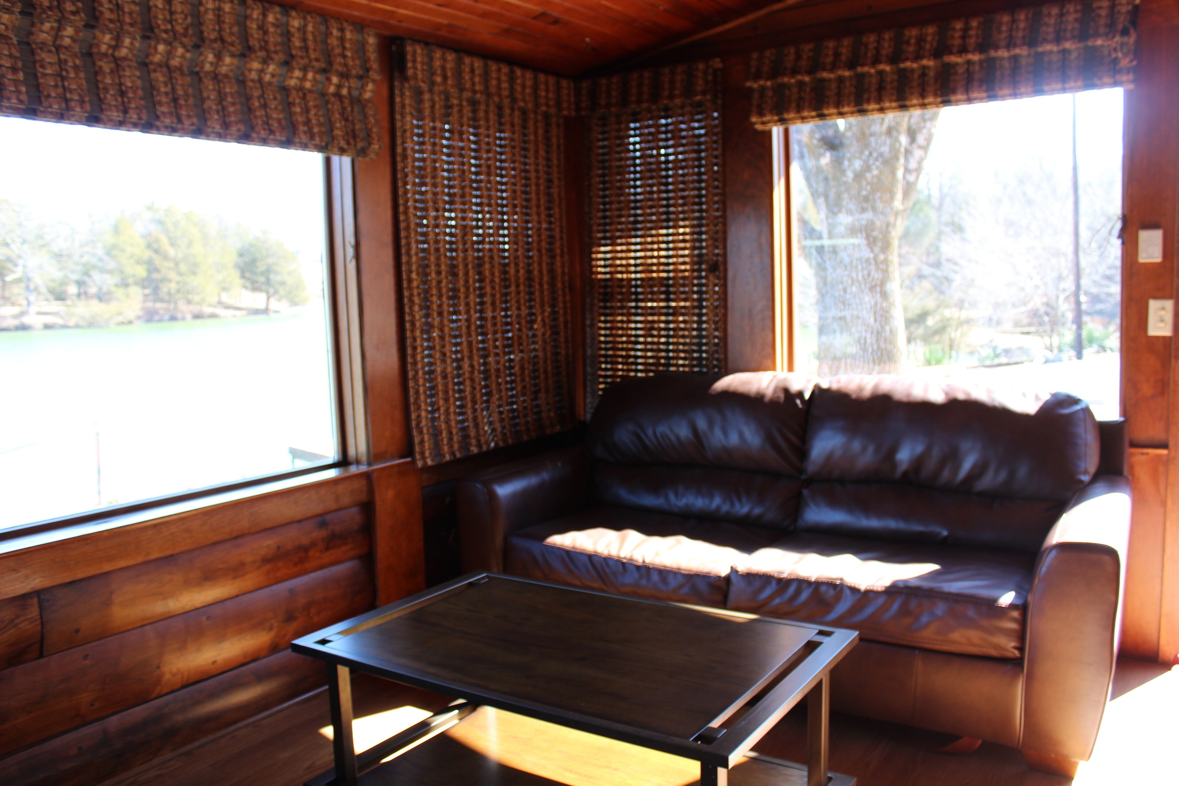 A room with a brown leather sofa, a wooden table, and a window with blinds.