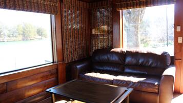 A room with a brown leather sofa, a wooden table, and a window with blinds.