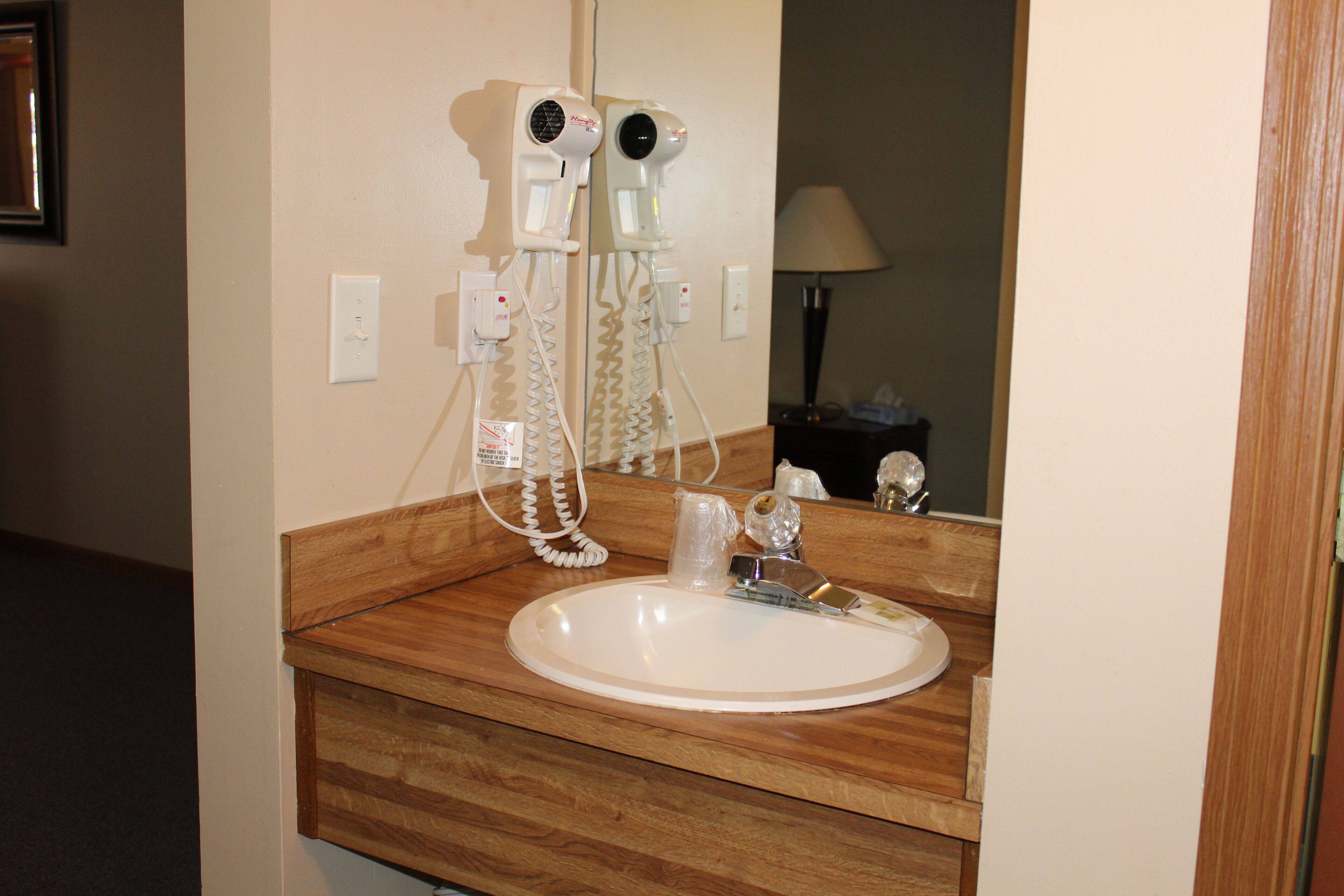 A bathroom with a wooden vanity, a white sink, and two hair dryers mounted on the wall.