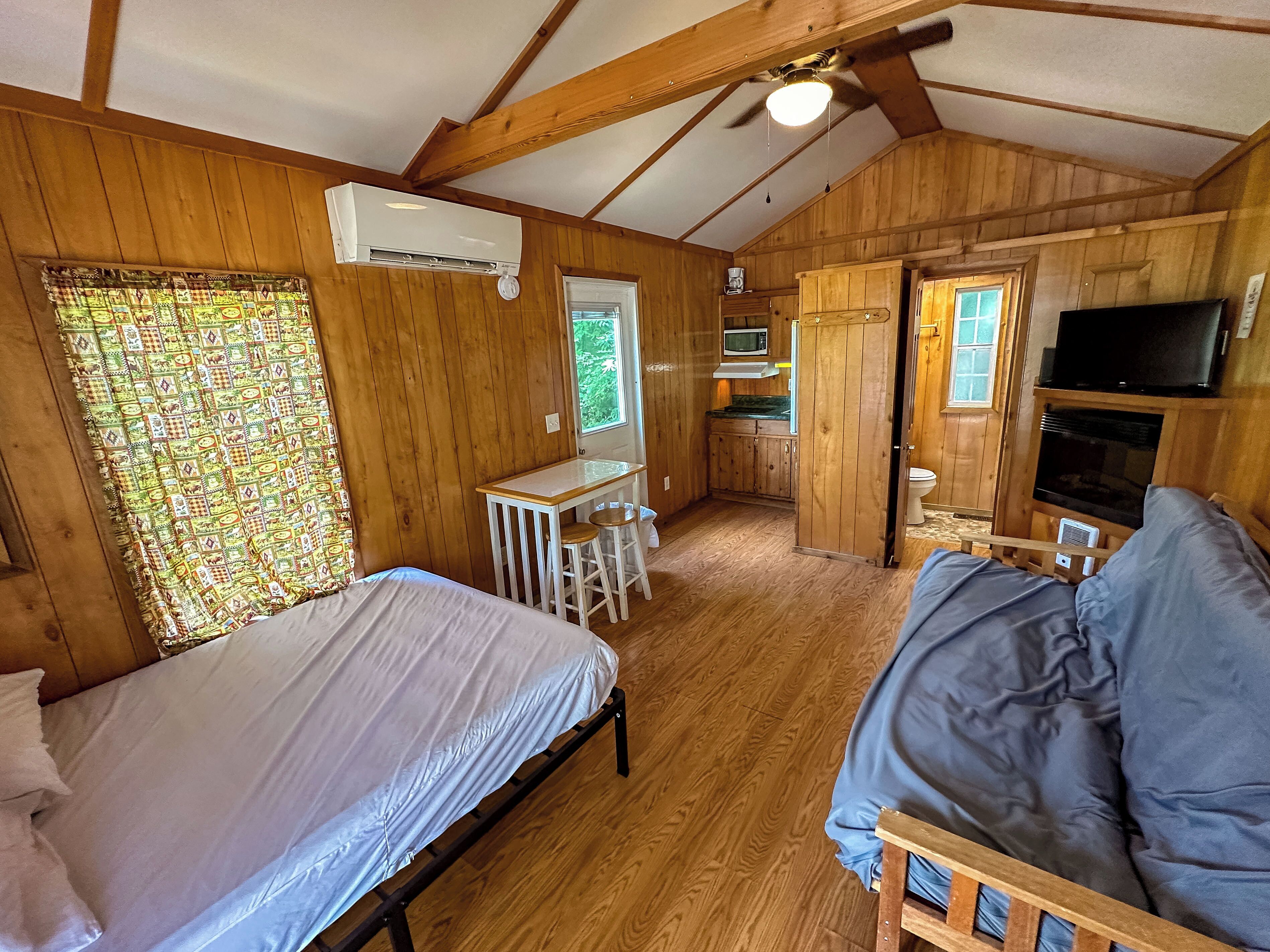 A compact cabin with a bed, a small kitchenette, a TV, and a ceiling fan.