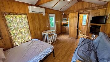 A compact cabin with a bed, a small kitchenette, a TV, and a ceiling fan.