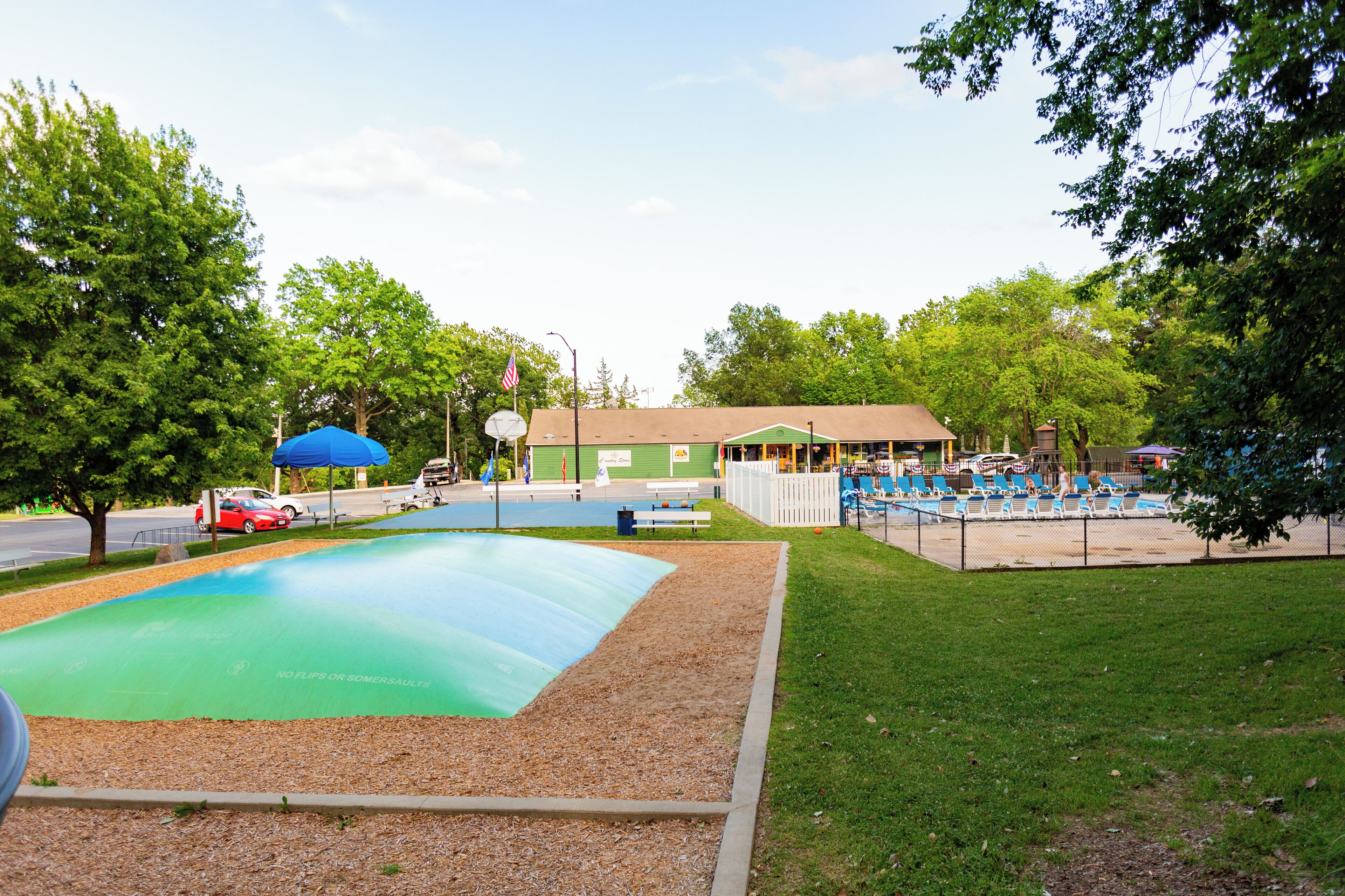 Une aire de jeux avec un toboggan vert, des chaises bleues et blanches, et une zone délimitée par une clôture.