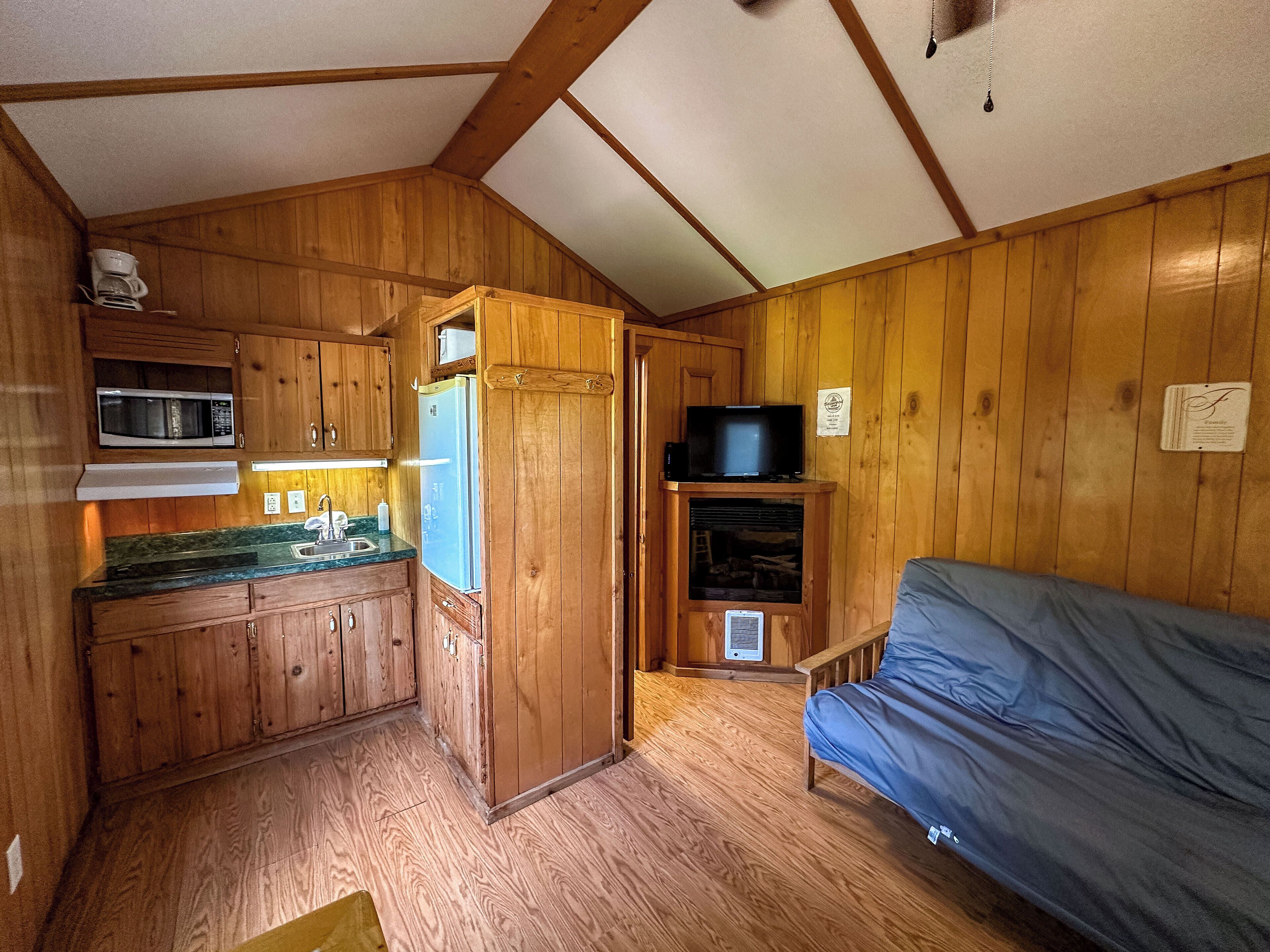 Ein gemütliches Blockhauszimmer mit Holzwänden, einer Küchenzeile, einem Fernseher und einem Bett.