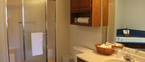 A bathroom with a glass-enclosed shower, a toilet, a sink with a mirror, and wooden cabinets.