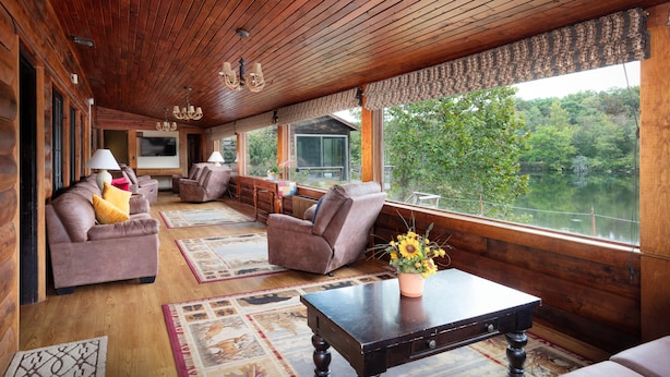 A wooden cabin interior with a sofa, armchairs, a table, and a view of a lake.