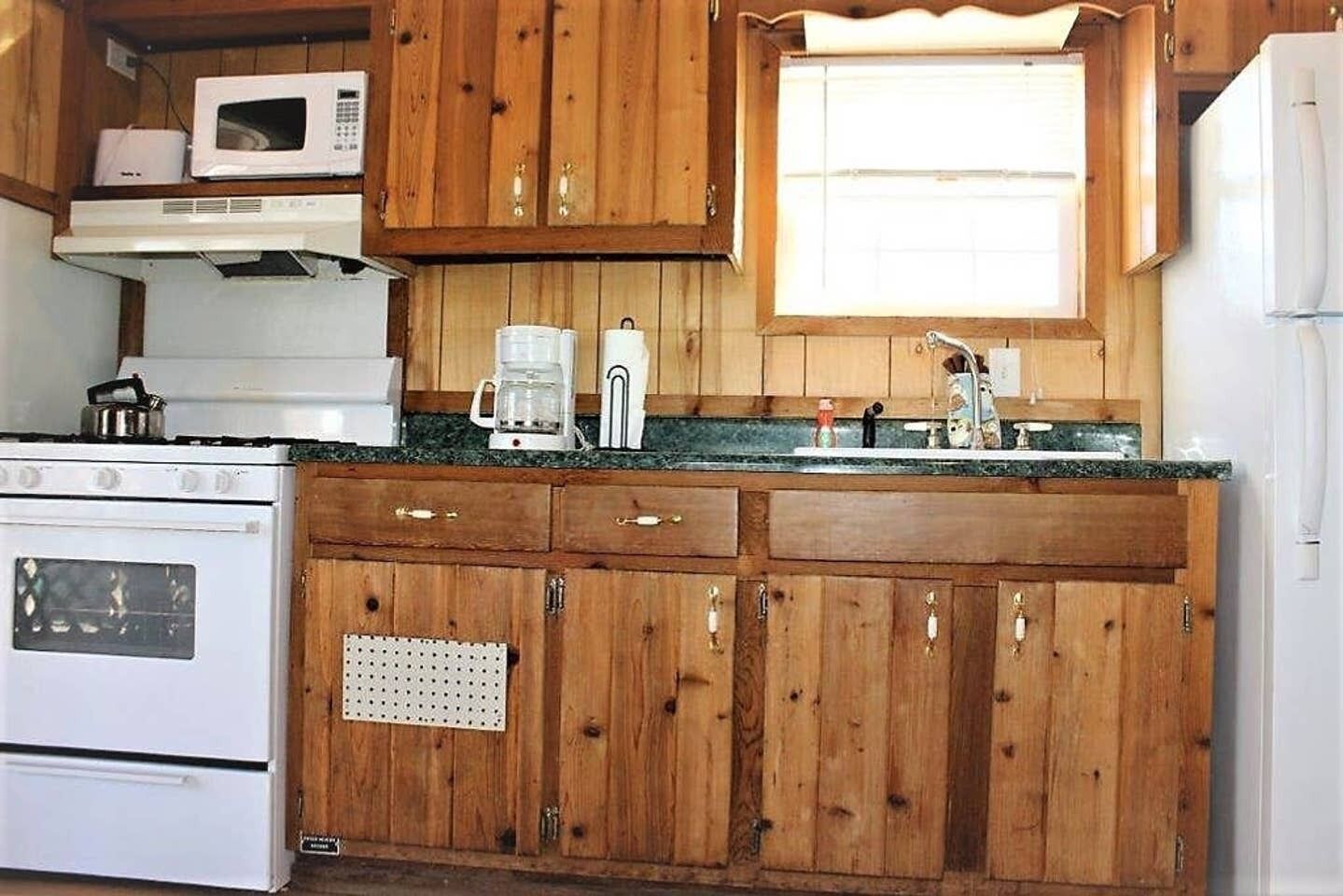 Una cocina con armarios de madera, estufa blanca, microondas, cafetera y un lavamanos.