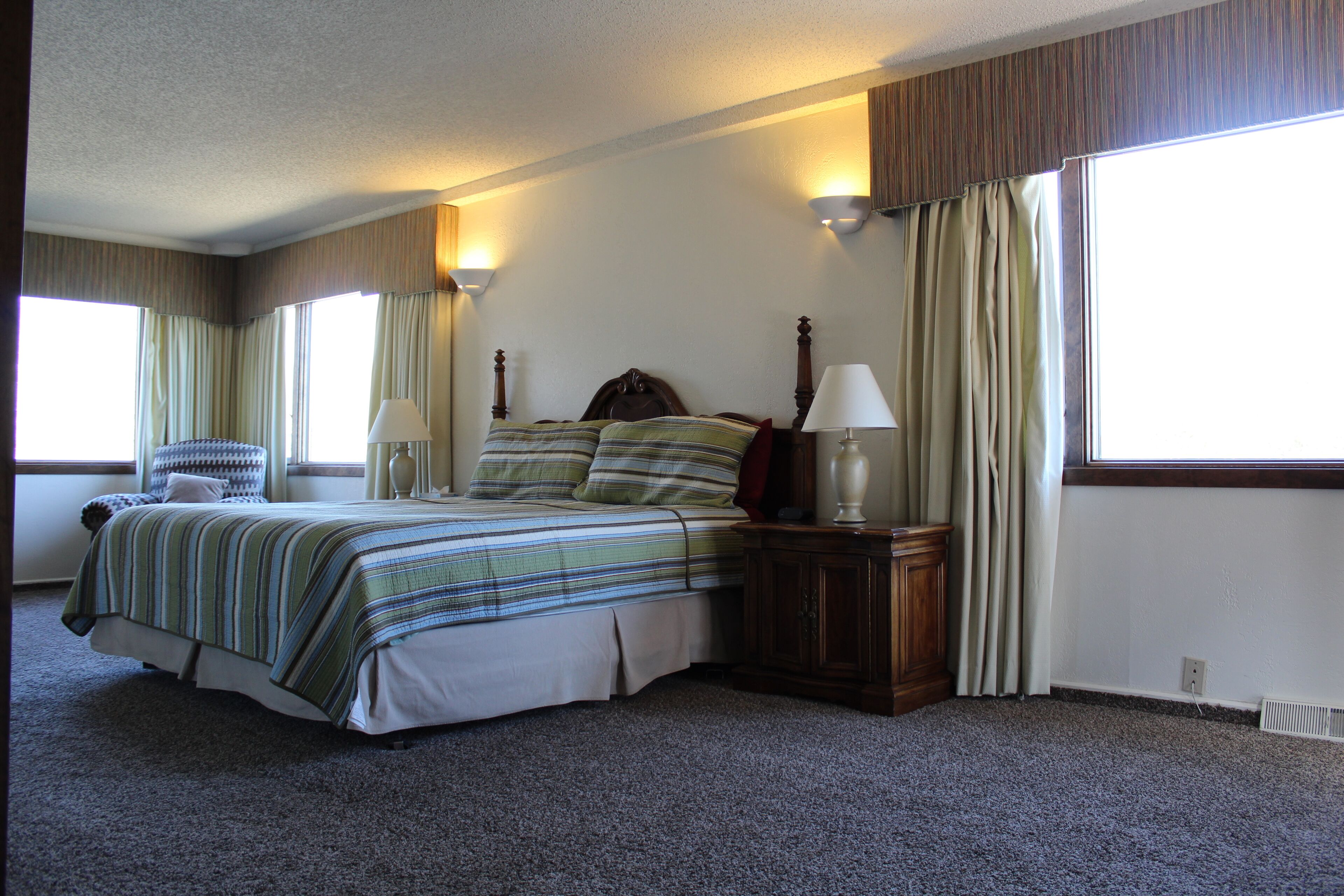 A bedroom with a large bed, two bedside tables with lamps, a chair, and a window with curtains.