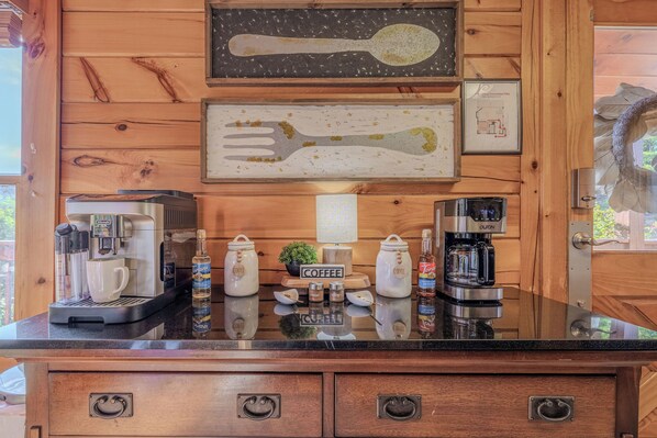 A wooden cabin interior with a kitchen counter, coffee makers, and a framed map on the wall.