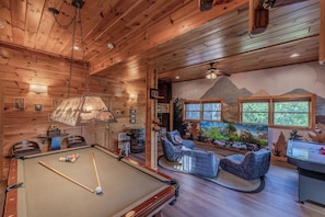 A wooden interior with a pool table, seating area, and a mural.