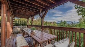 Terraza techada al aire libre con muebles de madera y vistas a montañas.