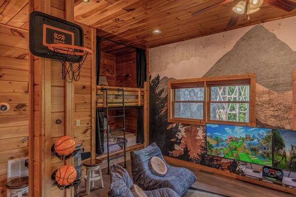 A room with a basketball hoop, bunk beds, a gaming console, and a mural.