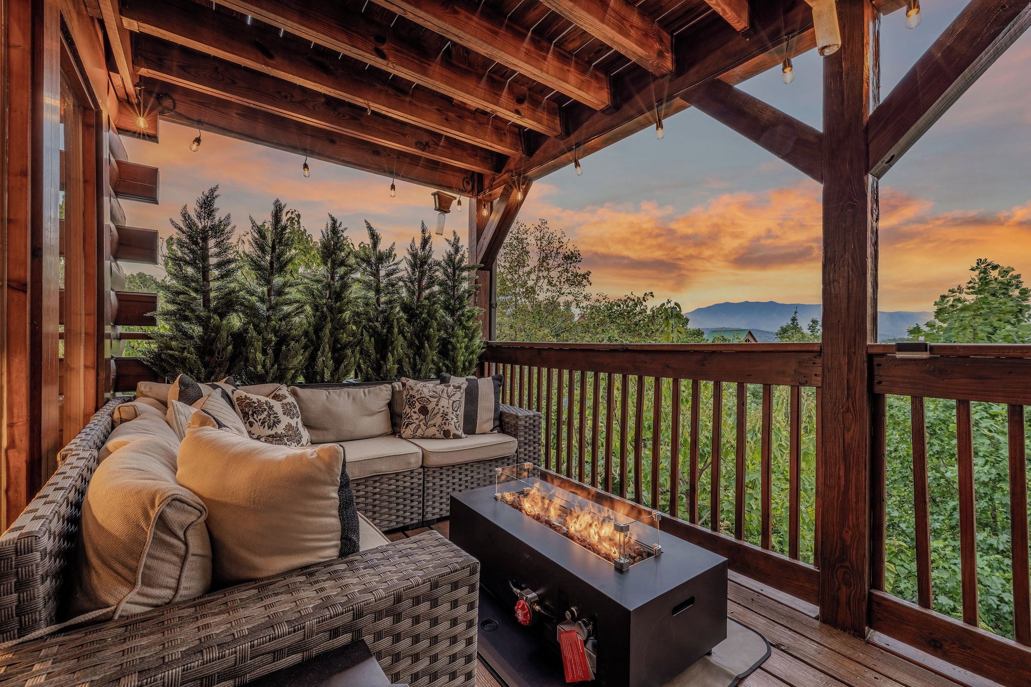A covered outdoor seating area with a fire feature, wooden beams, and a view of the landscape.