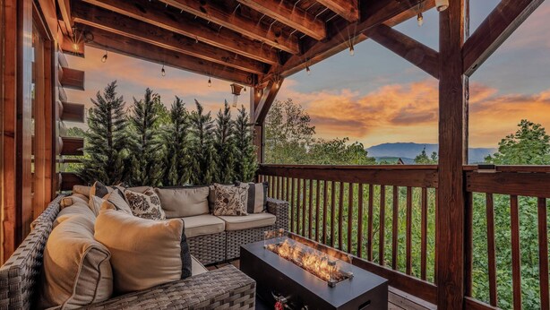 Un espacio de estar al aire libre techado, con una chimenea, vigas de madera y vistas al paisaje.