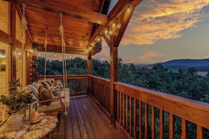 A wooden deck with a swing chair and a view of the surrounding forest.