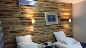 Habitación de hotel con dos camas, paneles de madera en la pared, un aire acondicionado instalado y dos lámparas fijadas a la pared.