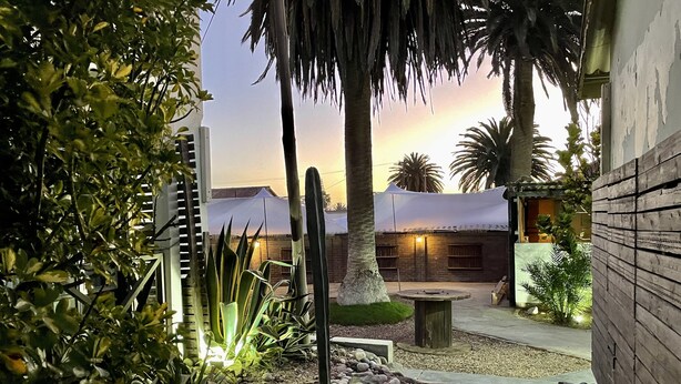 Un patio con sendero de piedra, palmeras y un edificio de ladrillo con toldo blanco.