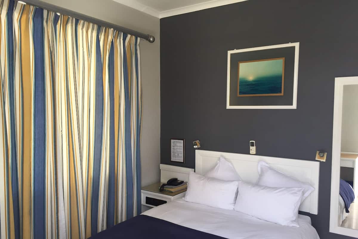 A hotel room with a bed, a nightstand, a painting on the wall, and a window with curtains.