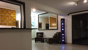 Un vestíbulo de hotel con un mostrador de recepción, un espejo grande y un letrero de neón que dice "CASAMIA".