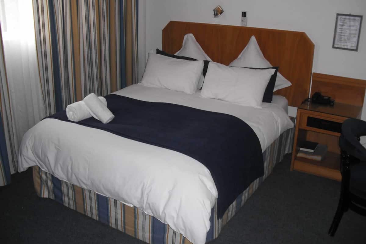 A hotel room with a bed, a nightstand, a chair, and a striped curtain.