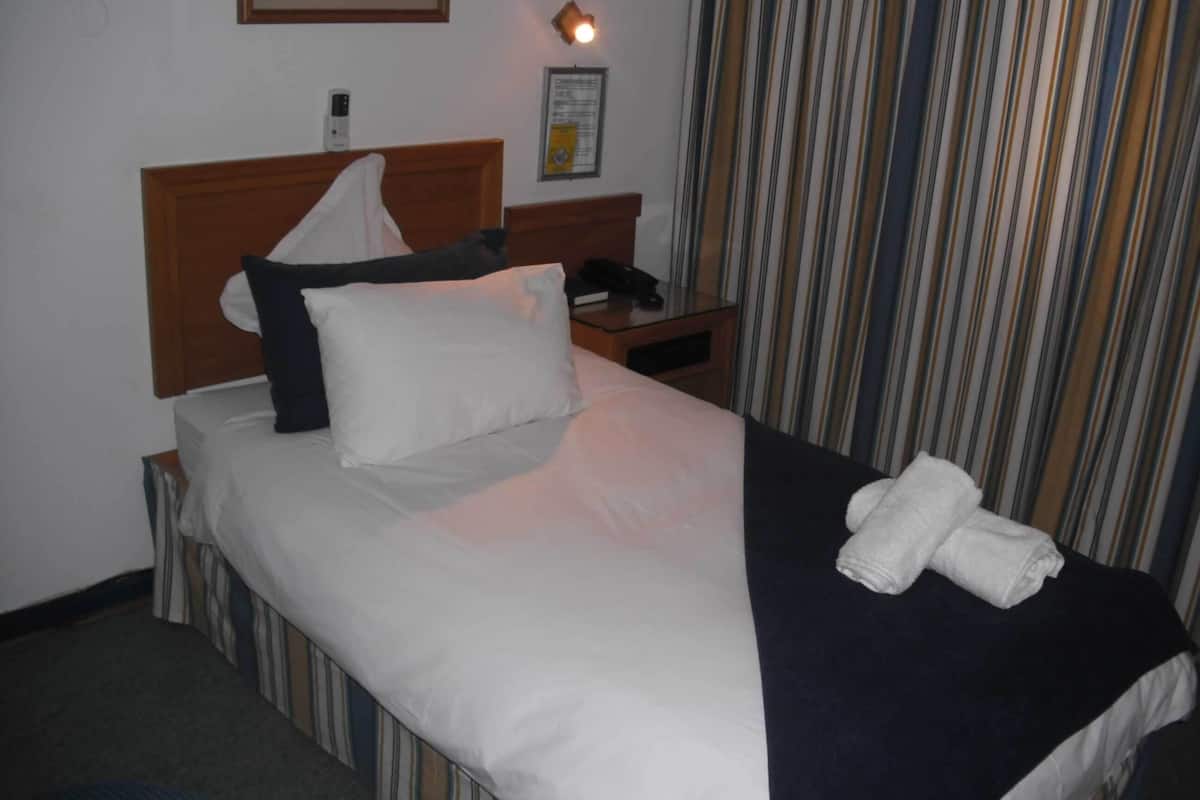 A hotel room with a neatly made bed, a bedside table with a lamp, a telephone, and a striped curtain.