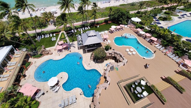 Un resort con varias piscinas, zonas de descanso y una playa.