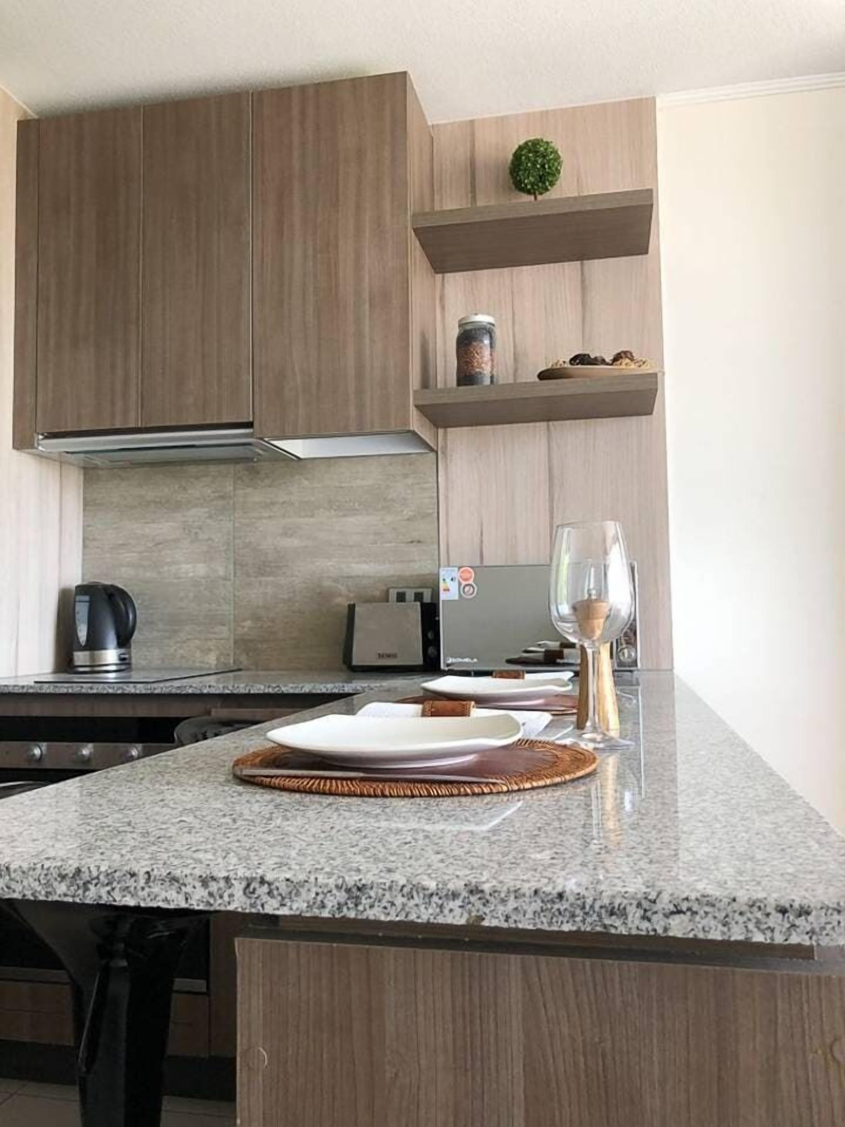 Une cuisine moderne dotée de plans de travail en granit, d’armoires en bois, d’un four encastré et d’un petit potager d’herbes aromatiques installé sur une étagère.