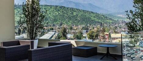 A balcony with wicker furniture and a view of a town and mountains.