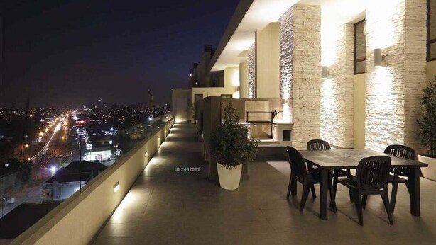 Un balcon avec une table et des chaises, un pot de fleurs et une vue sur le paysage urbain illuminé la nuit.