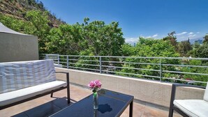 A balcony with a sofa, a table with a vase of flowers, and a view of greenery and buildings. - Bellavista Terrace, BBQ, Parking, AC & City view (Providencia)