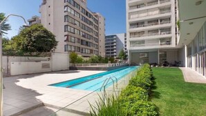 Un edificio moderno con piscina, rodeado de un césped cuidado y un cielo despejado.