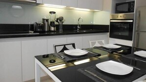 Una cocina moderna con armarios blancos, encimera negra y electrodomésticos de acero inoxidable.