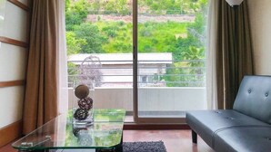 A room with a glass table, a sofa, and a view of greenery and buildings through large windows. - Bellavista Spotlight 1BR Apt - w/Parking & A/C (Providencia)