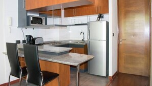 A compact kitchen with wooden cabinets, a microwave, a refrigerator, and a small dining area with two chairs. - Bellavista Spotlight 1BR Apt - w/Parking & A/C (Providencia)