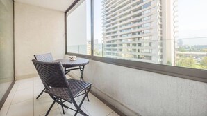 Ein Balkon mit zwei Korbstühlen und einem kleinen Tisch, mit Blick auf ein Hochhaus.