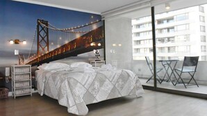 Ein Schlafzimmer mit einem großen Bett, einem Nachttisch, einer Lampe und Blick auf eine Brücke durch ein großes Fenster.