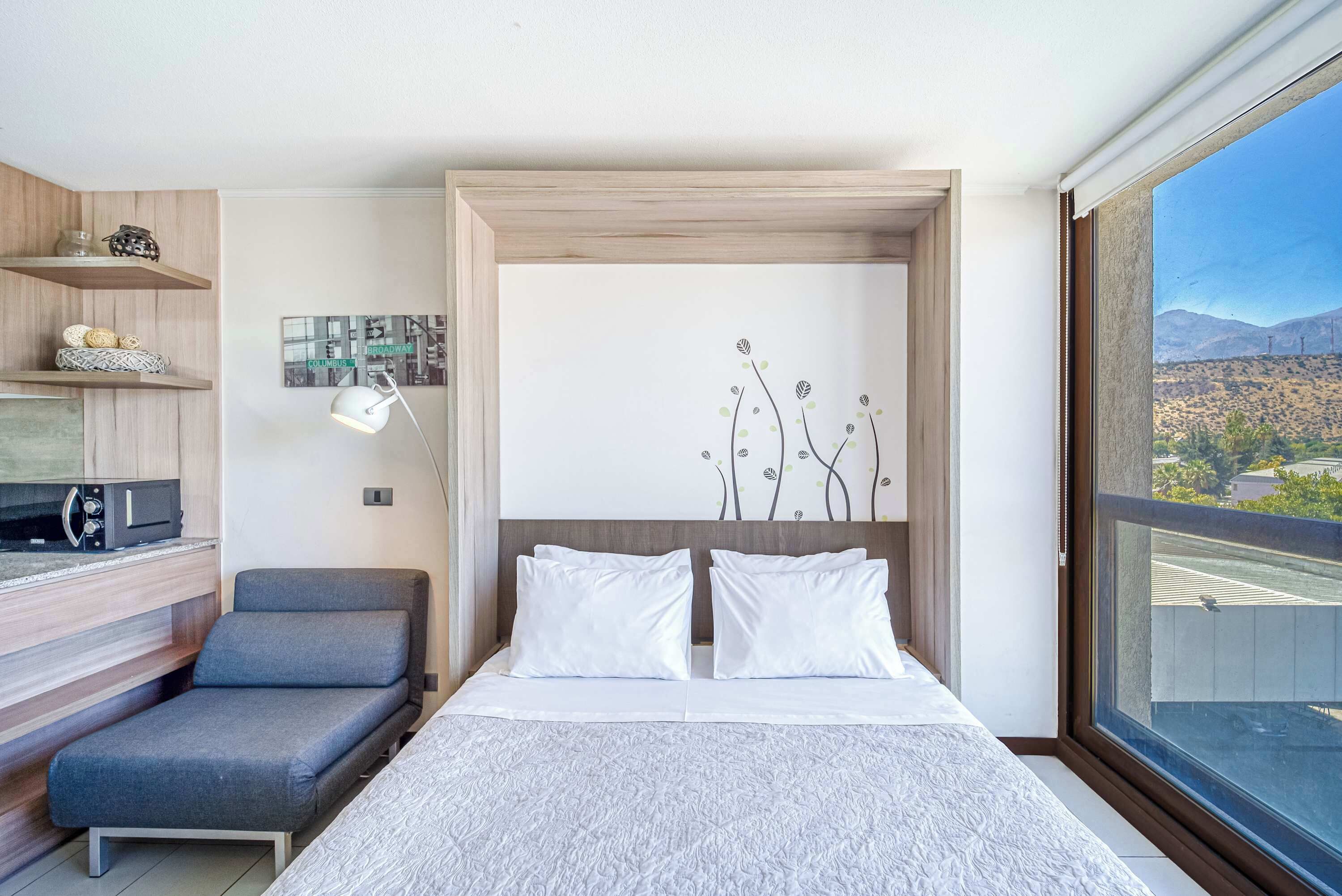 Un dormitorio moderno con cama, sofá, escritorio y un ventanal con vistas a las montañas.