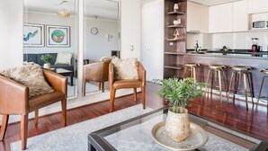 A modern living room with a glass coffee table, leather armchairs, and a large mirror.