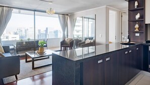 A modern living room with a glass coffee table, dark wood furniture, and a city view through large windows.