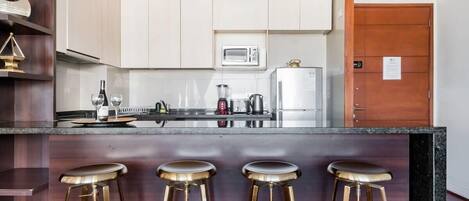 A modern kitchen with white cabinets, a microwave, a coffee maker, and a refrigerator. There are three stools at the counter.