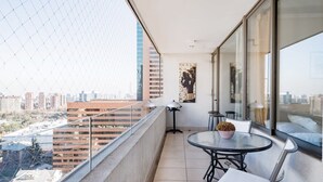 A balcony with a glass railing, a round table with chairs, a potted plant, and a city view.