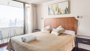 A hotel room with a large bed, a cityscape view, a wooden headboard, and a painting on the wall.