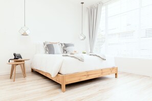 A minimalist bedroom with a wooden bed, a small bedside table with a phone, and a hanging light fixture. - A Home Away From Home (Comuna Chapinero)