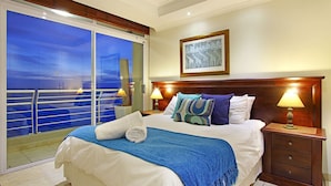 A hotel room with a large bed, two bedside tables with lamps, a framed picture on the wall, and a balcony with a railing. - Ocean View C602 bt HostAgents (Cape Town)
