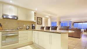 A modern kitchen with a built-in oven, a coffee maker, and a dining area with a large window. - Ocean View C602 bt HostAgents (Cape Town)