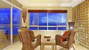 A balcony with wicker furniture, a table, and a view of the city at dusk. - Ocean View C602 bt HostAgents (Cape Town)