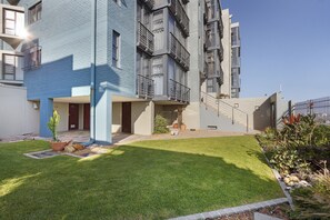 A modern multi-story residential building with a well-maintained lawn and potted plants.